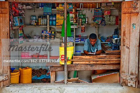 Tanzanie, Zanzibar. Un commerçant lit pendant que vous attendez de clients à son atelier de petit village de Nungwi.