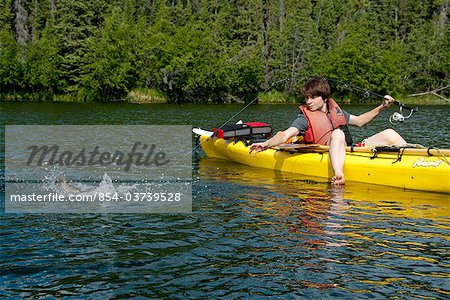 Boy catching Rainbow trout from his sea kayak at  Silver Lake in Wrangell-St. Elias National Park, Southcentral Alaska, Summer