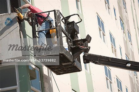 Male worker installs siding during renovation of McKinley Tower aprtments (formerly the MacKay Building) in downtown Anchorage, Southcentral Alaska, Summer