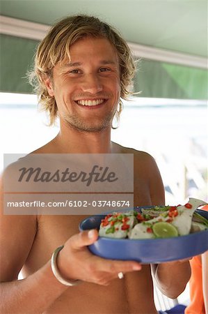A smiling man holding a plate of marinated fish.
