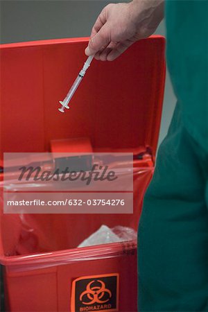 Healthcare professional placing used syringe in hazardous waste receptacle