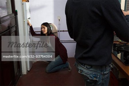Woman with stomachache crouching before refrigerator