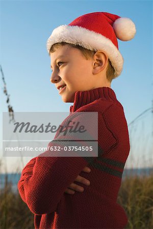 Boy wearing Santa hat outdoors, contemplatively looking away