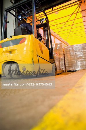 Forklift operator loading wrapped pallets of cardboard boxes onto trailer in warehouse