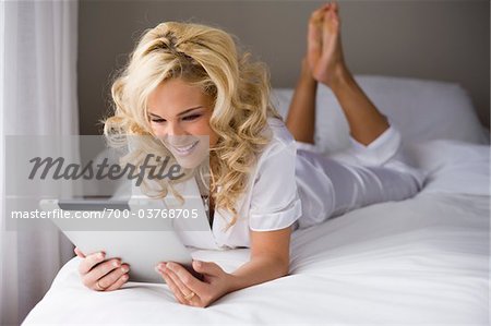 Woman Lying on Bed Using Electronic Tablet