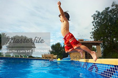 Young boy jumping into swimming pool