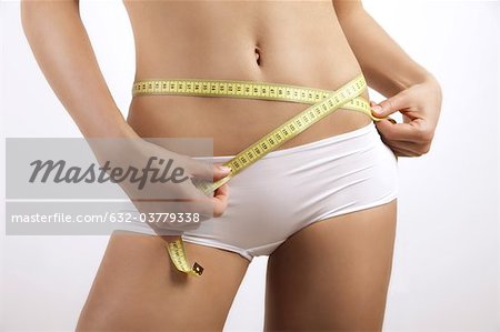 Young woman measuring hips with measuring tape, cropped
