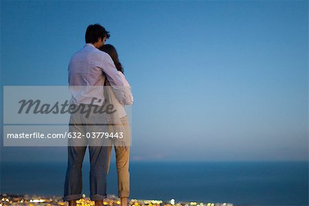 Couple debout sur le bord de la piscine à débordement au crépuscule, à la recherche en mer