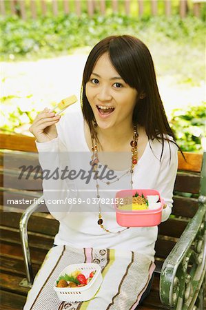 Young Woman Sitting on Bench and Eating Lunch
