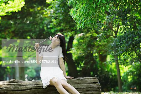 Junge Frau sitzend auf Baumstamm hält Blume