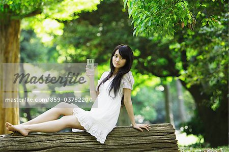 Junge Frau sitzend auf Baumstamm mit Glas Wasser