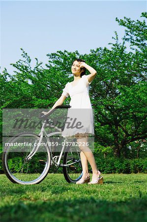 Jeune femme debout tenant un vélo dans le parc