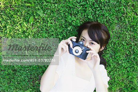 Young Woman Lying on Grass Holding Camera