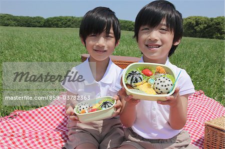 Twins Sitting Holding Lunch Boxes in Park