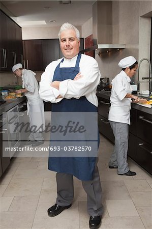 Chef stands avec bras plié en tablier bleu et organisé de cuisine