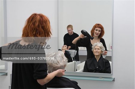 Stylist blow-drys elderly woman's hair