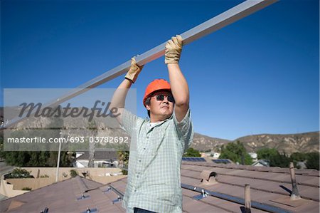 A man lifting a large metal pole on a roof top