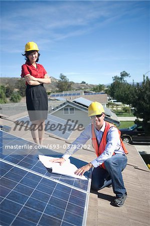 Two business people on a rooftop next to solar panelling with a set of plans