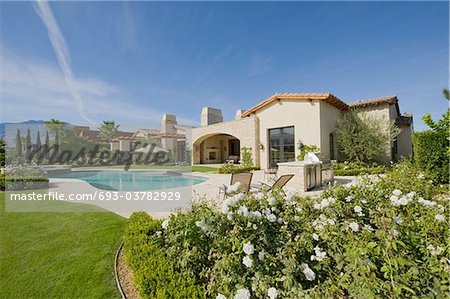 Extérieur de la maison en plein jour, avec un jardin, une piscine avec des plantes et des collines dans le lointain