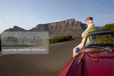 Senior man admires view leaning on vintage racing car on Signal Hill, Cape Town, South Africa