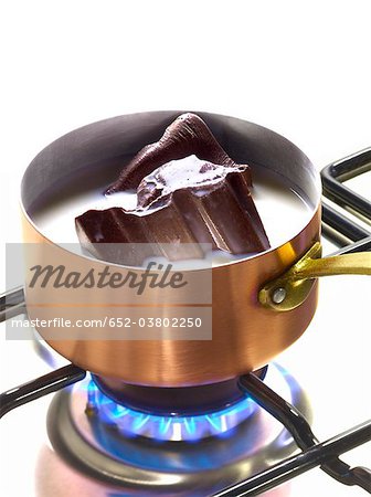 Melting pieces of chocolate in milk in a copper saucepan