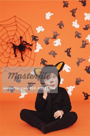 Boy In Cat Costume For Halloween Sitting Against Orange Background