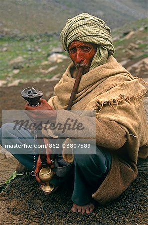 India, Himachal Pradesh, Chamba Valley. A Gaddi (semi-nomadic shepherd) from Chamba smokes a hookah, or water pipe, on the trail linking Kugti village, Kugti Pass and the summer grazing meadows of Lahaul.