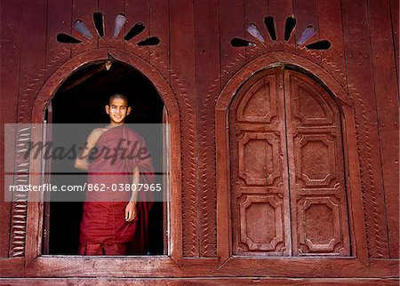 Myanmar, Burma, Nyaungshwe.  A young novice monk standing at a wooden window, Shwe Yaunghwe Kyaung monastery.