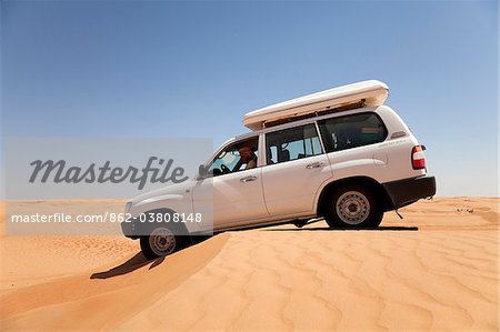 Oman, Wahiba Sands. A 4x4 eases over a sand dune in the midday sun.