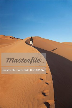 Oman, vide. Une jeune femme fait son chemin jusqu'à les dunes abruptes.