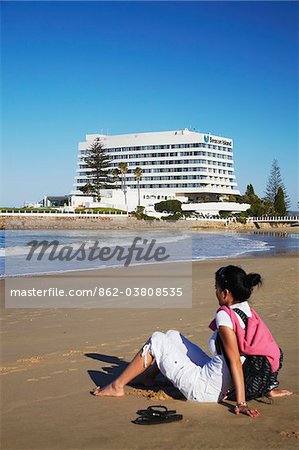 Femme relaxante sur la plage avec Beacon Island Hotel à fond, Plettenberg Bay, Western Cape, Afrique du Sud Femme relaxante sur la plage avec Beacon Island Hotel à fond, Plettenberg Bay, Western Cape, Afrique du Sud