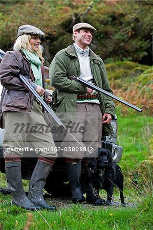 North Wales, Snowdonia ; Gilar Farm. A man and woman relax leaning against their landrover whilst out shooting.