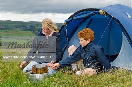 UK, North Wales, Snowdonia.  Two children cook on a campstove while camping