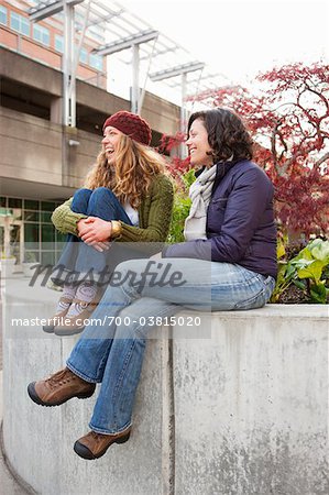 Zwei Frauen auf Zement Mauer sitzen und lachen