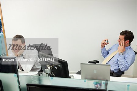 Businessman using smartphone, male colleague looking sideways