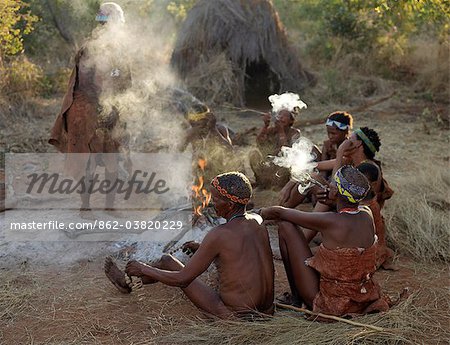 Un groupe de NIIS chasseurs cueilleurs s'asseoir autour leur feu et la fumée.Ils font partie du peuple San, souvent appelé comme Bushmen.They diffèrent par l'apparence du reste de l'Afrique noire peau jaunâtre et légèrement désossées, maigre et musclé.Ils vivent dans l'environnement hostile d'une vaste étendue de sable plat et bush gommage pays cheval sur la frontière de la Namibie Botswana.