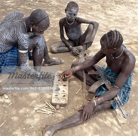 Two Mursi men with singular hairstyles play a game of bau as a young boy watches them. Most men possess rifles to protect their families from hostile neighbours.Body art is an important aspect of Mursi culture.They live in a remote area of southwest Ethiopia along the Omo River.