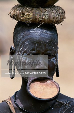 A woman of the Mursi tribe. Once married Mursi women pierce their lower lip and stretch it by inserting  increasingly large plugs until they can wear a clay lip plate. The size of the lip plate reflects the bride price paid by their husband. Within the Omo Valley, the Mursi have a reputation for being extremely fierce and aggressive but also for their skill at making pots. This women carries a pot