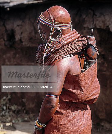 A Samburu bride waits pensively outside her new home until she is enticed in with promises of cattle.Her wedding gown is made of three goatskins, which are well oiled and covered in red ochre.She carries on her back a gourd full of milk and a small wooden jar containing butter.She now wears the mporro necklace of married women.