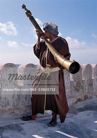 A Swahili man in traditional attire blows the Siwa on the battlements of the Lamu Museum.This unique and hugely heavy ritual horn was used before the 19th century in Pate and Lamu Islands to herald religious and festive occasions or to alert the community of danger.