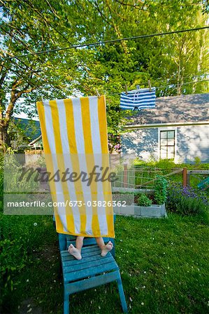 garçon sur chaise de jardin sous la serviette de plage