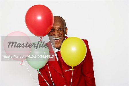 A middle-aged man wearing a red suit and holding balloons.