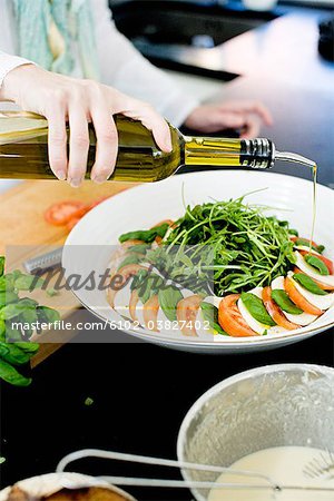 A hand pouring a bottle  of olive oil over tomatoes and mozzarella.