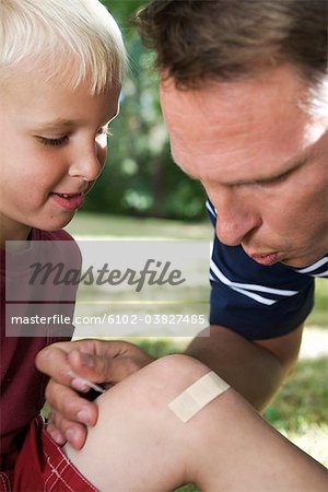 A father putting on a plaster on the knee of his son, Sweden.