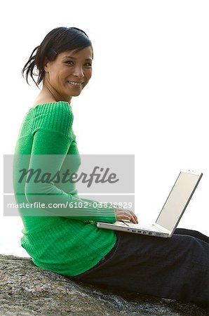 Une jeune femme sur un rocher à l'aide d'un ordinateur portable, Suède.