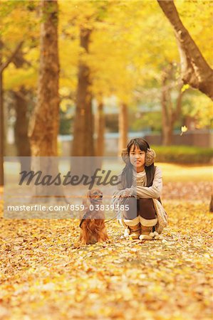 Fille accroupie avec mascotte chien dans le feuillage d'automne