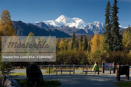 Femme est assise sur un banc avec vue sur le secteur sud du Mt. McKinley et chaîne de l'Alaska de l'aire de repos de mémorial de l'ancien combattant de l'Alaska le long de la route de George Parks, centre-sud du parc national Denali en Alaska, automne