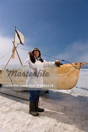 Männliche Inupiak Eskimo Jäger stehen neben einem Inupiaq Umiaq gemacht während des Tragens einer traditionellen Eskimo Parka (Atigi) und Siegel Haut Hut, Tschuktschensee in der Nähe von Barrow, Alaska Arctic Sommer Bartrobbe Haut (Ugruk)