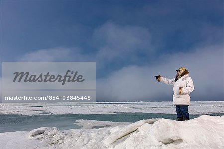 Male Inupiaq Eskimo hunter standing on a ice pressure ridge while wearing a traditional Eskimo parka (Atigi) and seal skin hat, Chukchi Sea near  Barrow, Arctic Alaska, Summer