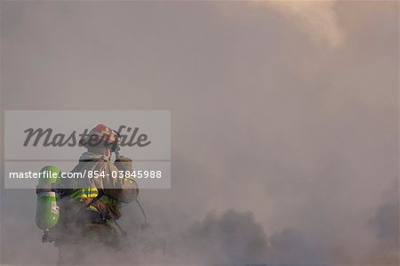 An Anchorage Fire Department firefighter stands atop the roof of a downtown motel while working to extinguish the blaze, Southcentral Alaska, Winter